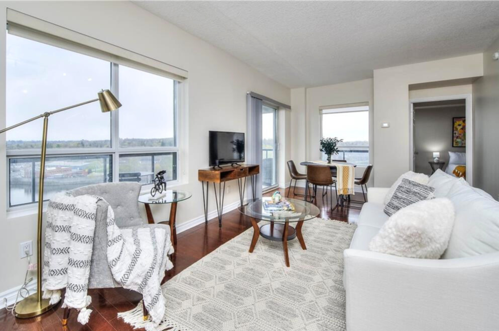 A condominium with pristine white walls, elegantly styled by Helen's Team, showcasing a white couch, a matching carpet, and tasteful accents dispersed throughout the space.