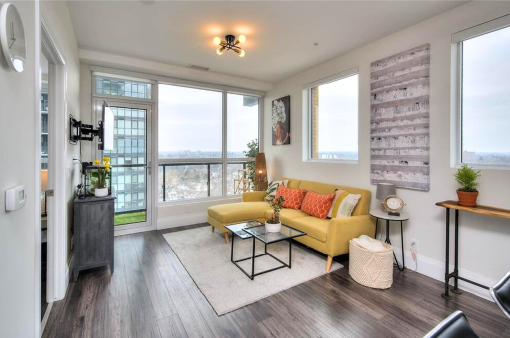 Condominium living room expertly staged by Helen's Team, featuring glass windows and a vibrant yellow couch adorned with tasteful accents.