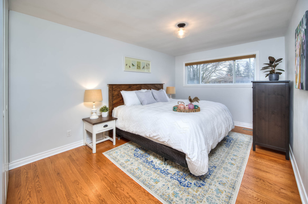 A tastefully decorated bedroom featuring a plush bed set against a minimalistic interior design. The room includes a cozy carpet, a sleek bedside lamp, and is an epitome of Helen's Design's staging expertise.