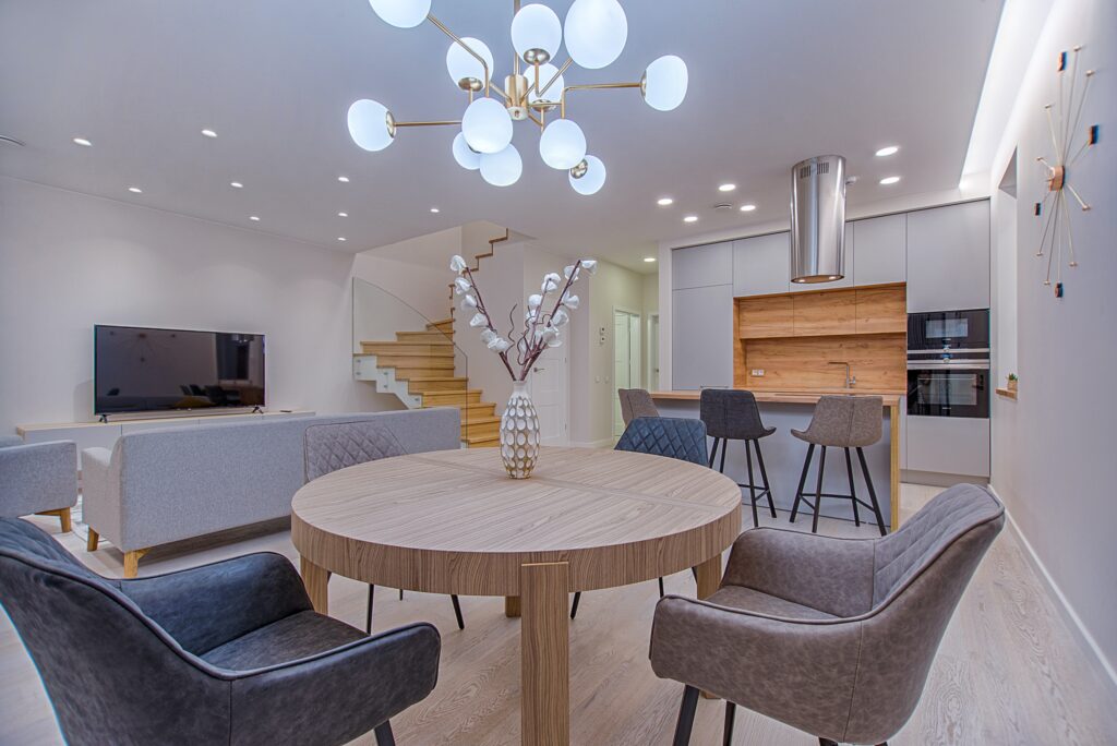 A contemporary living room and dining area adorned with gray accents, illuminated by a modern chandelier, creating a bright and inviting ambiance.