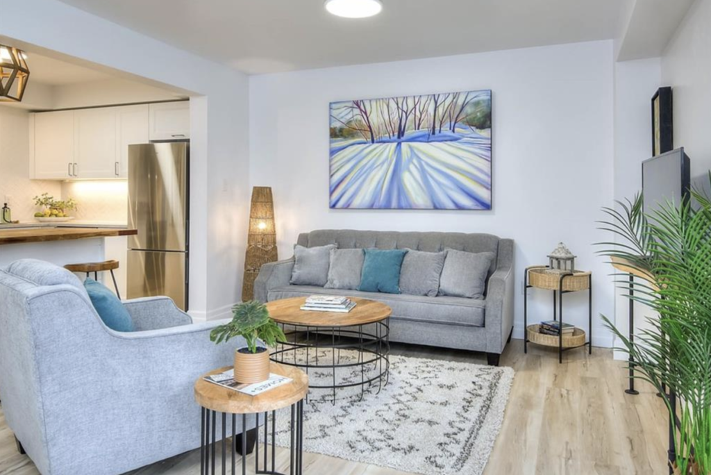 Living room with gray couches, blue accent pillow, decorative plants, and coffee table, staged by Helen's Design.