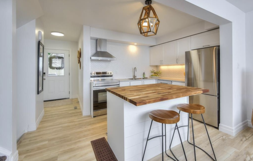 Staged kitchen with island table featuring wooden top, refrigerator, wooden stool, and more, designed by Helen's Design