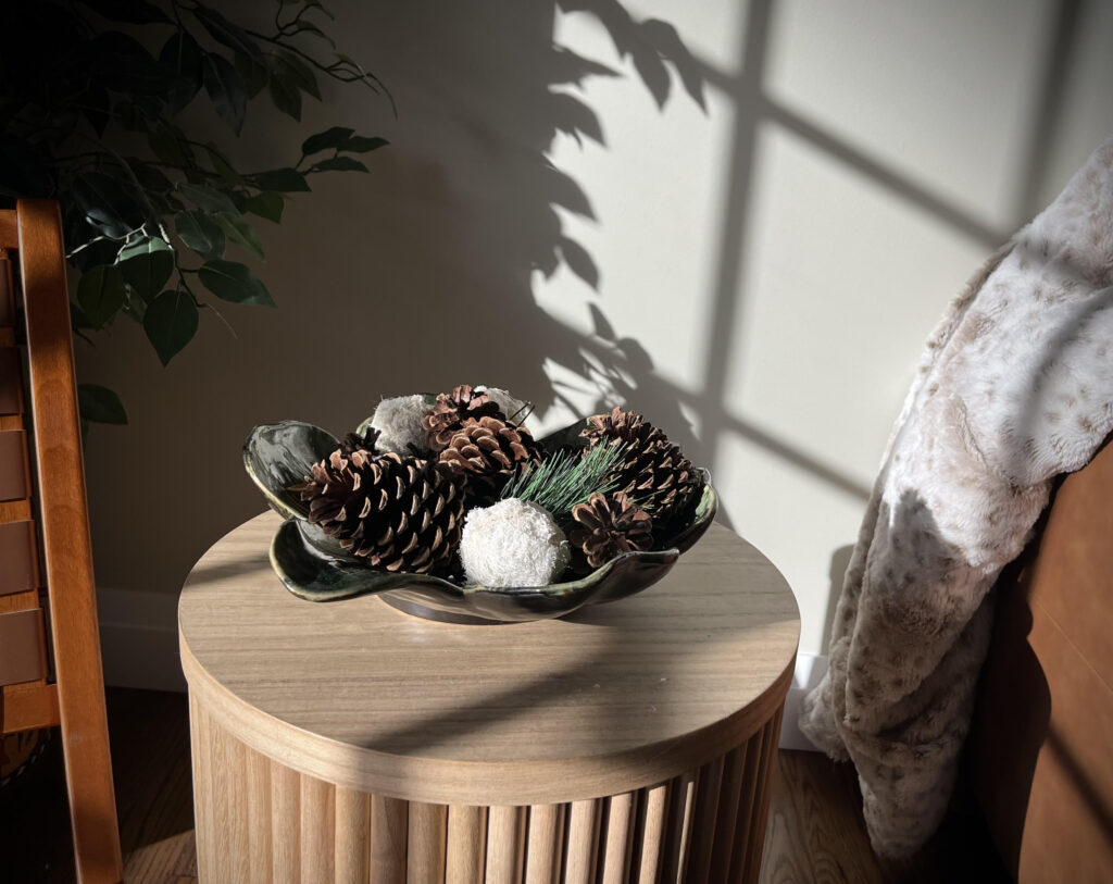 A wooden side table featuring a decorative vase filled with a pinecone and sprigs of leafy accents, creating a cozy and natural aesthetic.